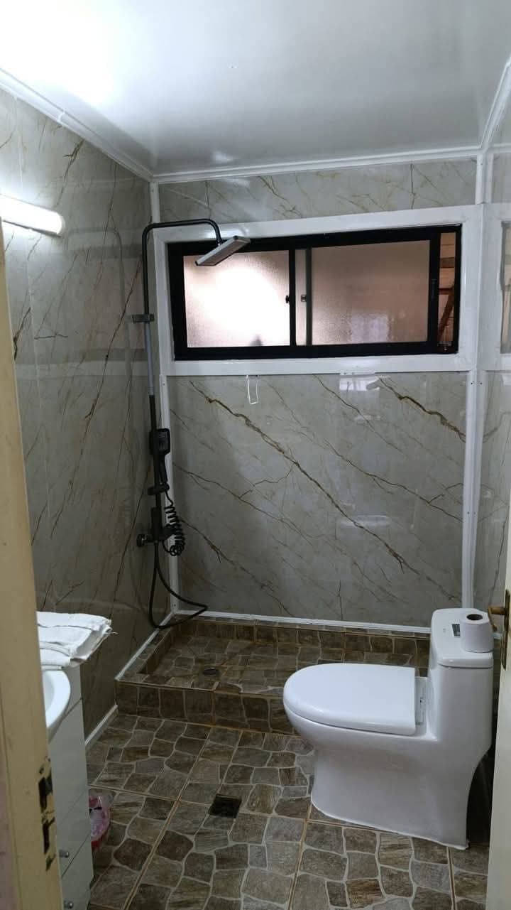 Baño pequeño con paredes de mármol, ducha negra, inodoro blanco y suelo de baldosas rústicas.