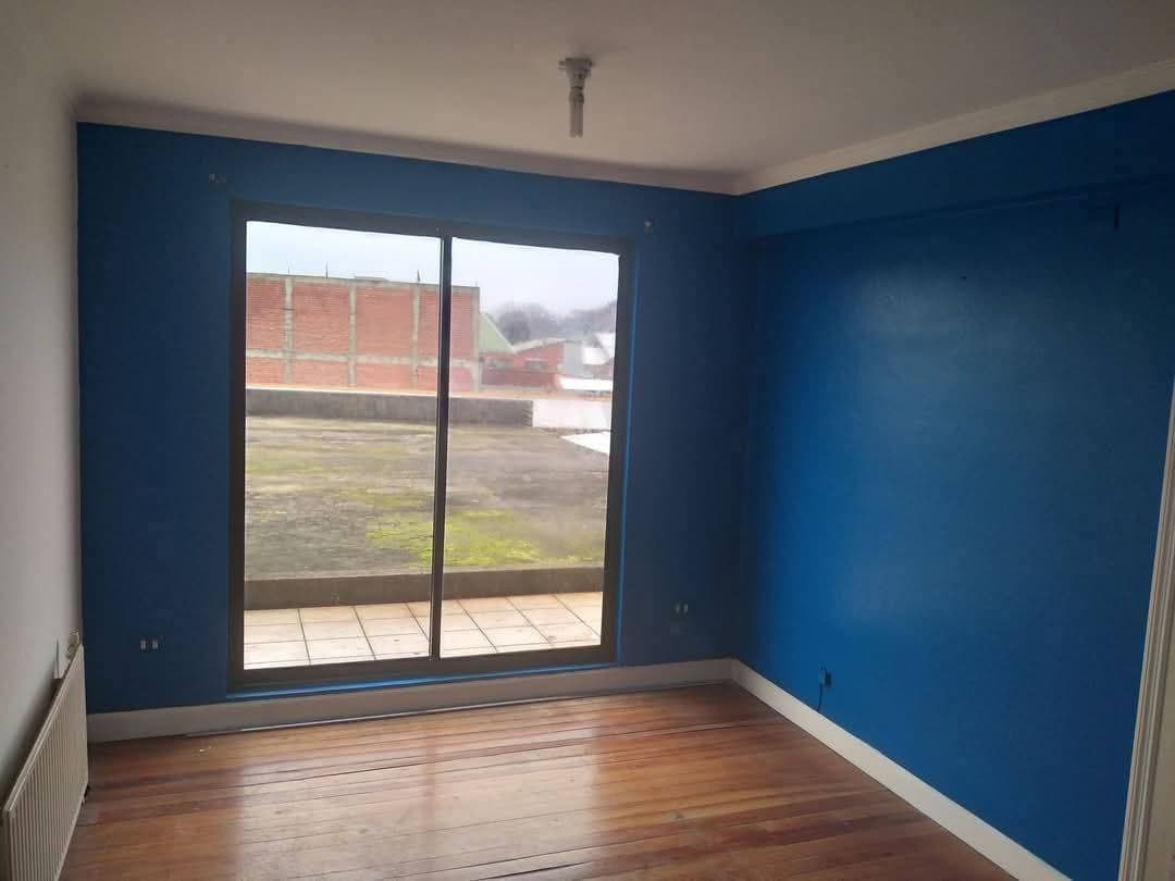 Habitación vacía con paredes azules, piso de madera y gran ventanal hacia una terraza exterior.
